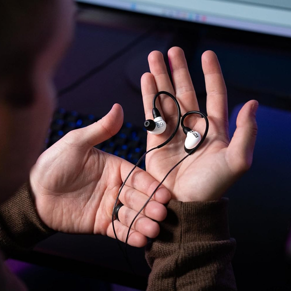 Person holding a pair of earbuds in front of a computer screen
